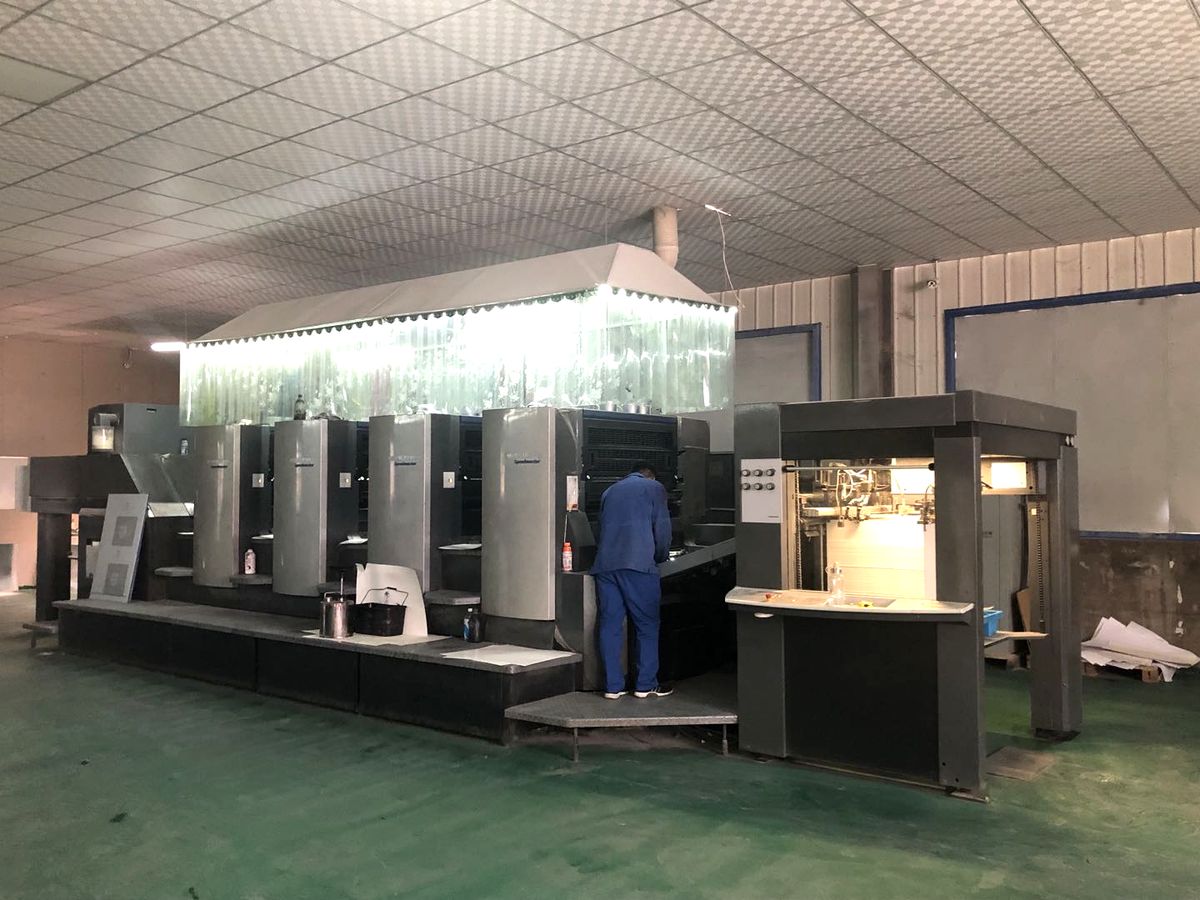 Multi-colour offset printing press running matchbox board, with operator at the delivery end